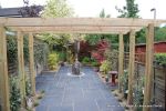Small town house garden with a Japanese feel black limestone random paving installed with a centre slate water feature, Timber arbour constructed and garden planted with feature plants  